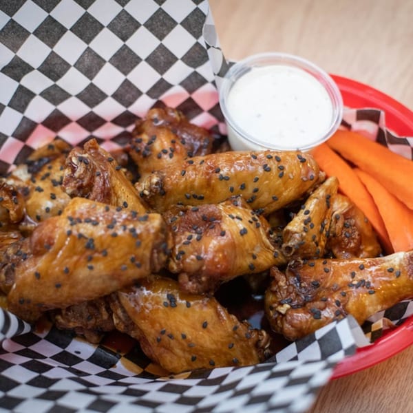 Legends Grill's sesame chicken wings with ranch dip and carrot sticks in a red basket.