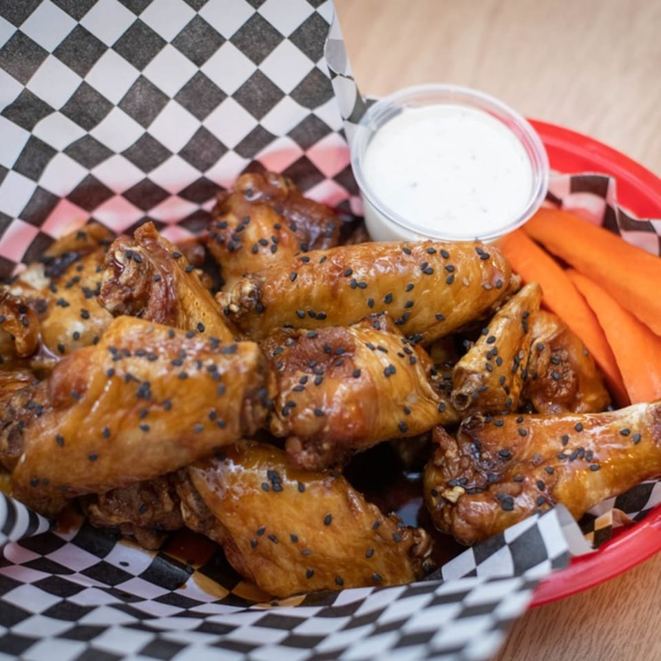 Legends Grill's sesame chicken wings with ranch dip and carrot sticks in a red basket.