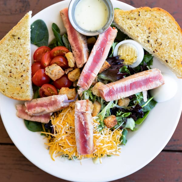 Seared tuna salad with cherry tomatoes, croutons, shredded cheese, hard-boiled egg, and garlic toast.