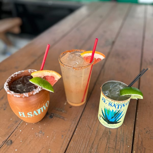 Three El Sativo tequila cocktails, two garnished with grapefruit and lime, on a rustic wooden table.