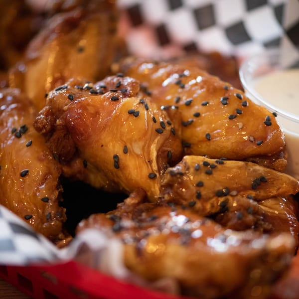 Legends Grill's sticky, glazed chicken wings with black sesame seeds in a red basket with dip.
