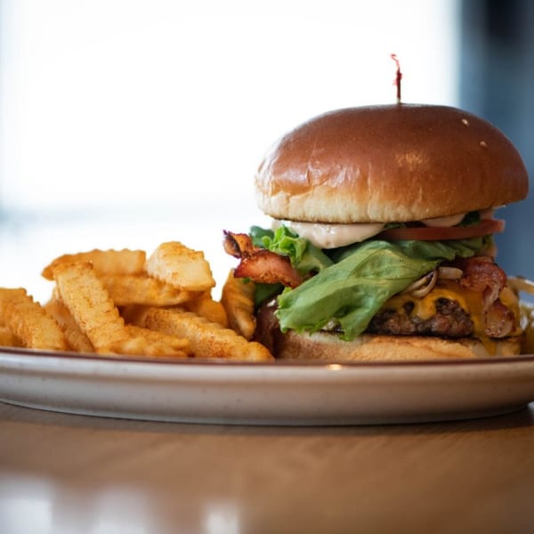 A Legends Grill bacon cheeseburger with lettuce, tomato, and sauce, served with crinkle-cut fries.