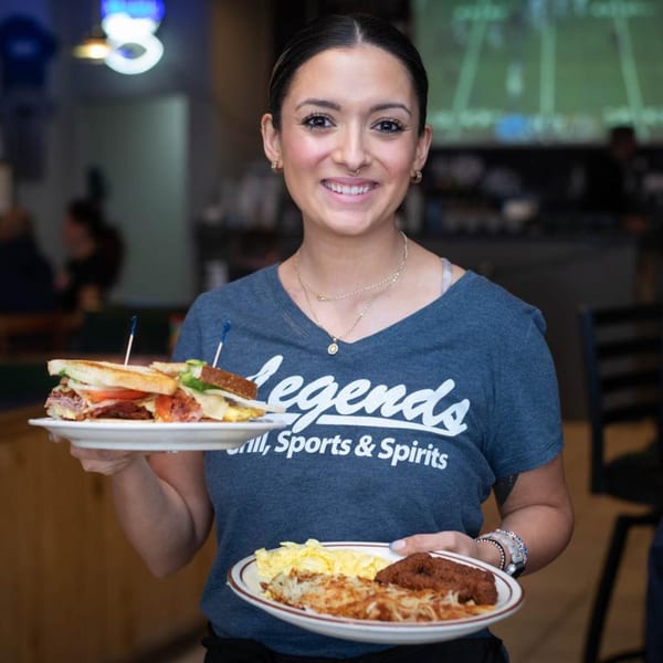 Legends Grill server holding a sandwich, hash browns, scrambled eggs, and sausage patties.