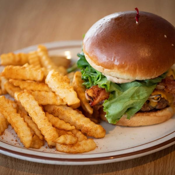 A Legends Grill burger with lettuce, cheese, and bacon, served with seasoned crinkle-cut fries.