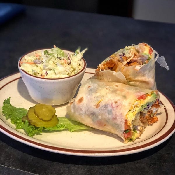 Legends Grill Sports & Spirits' chicken wrap with coleslaw, lettuce, and pickles on a plate.