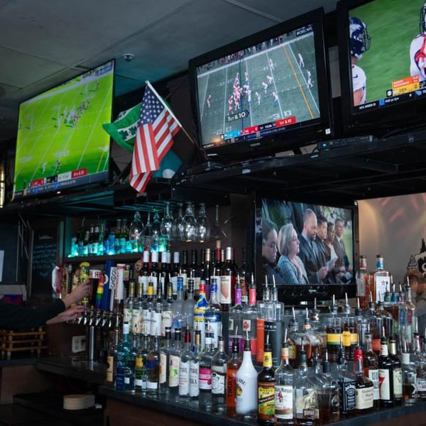 A sports bar with multiple TVs showing football games above a fully stocked bar with a bartender.